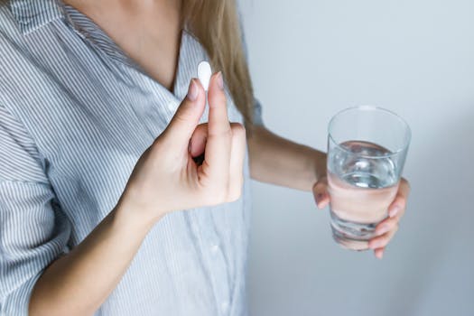 pexels-photo-576831-576831 Close-up of a woman holding a pill and a glass of water, ready to take medication.
